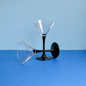 Two clear martini glasses with black stems on a blue background