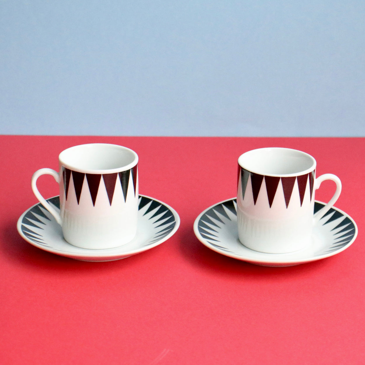 Two ceramic cups with saucers on a red surface with a light blue background