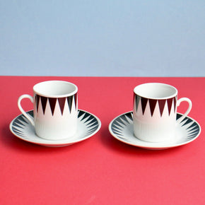Two ceramic cups with saucers on a red surface with a light blue background