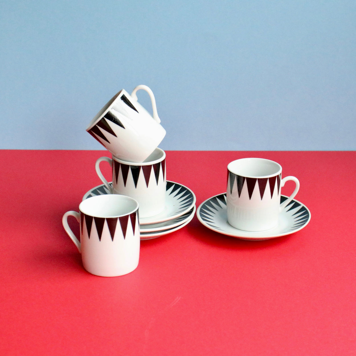 Set of white cups with black geometric patterns on saucers against a red and blue background