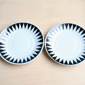 Two black and white patterned saucers on a beige surface