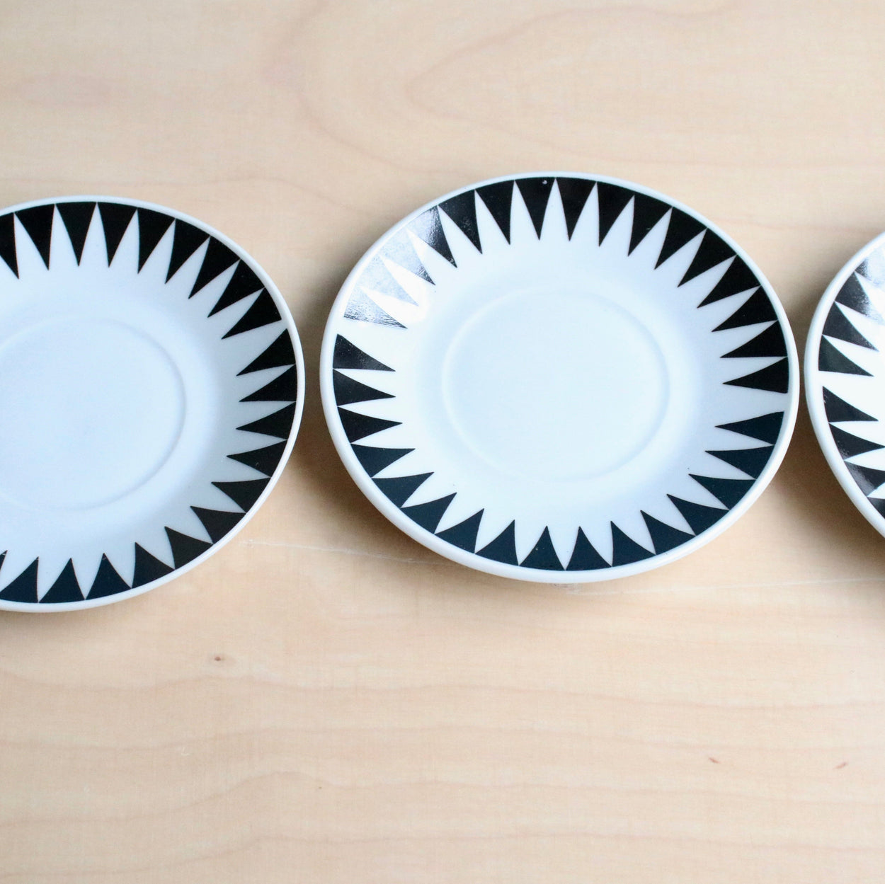 Three ceramic plates with black geometric patterns on a beige surface