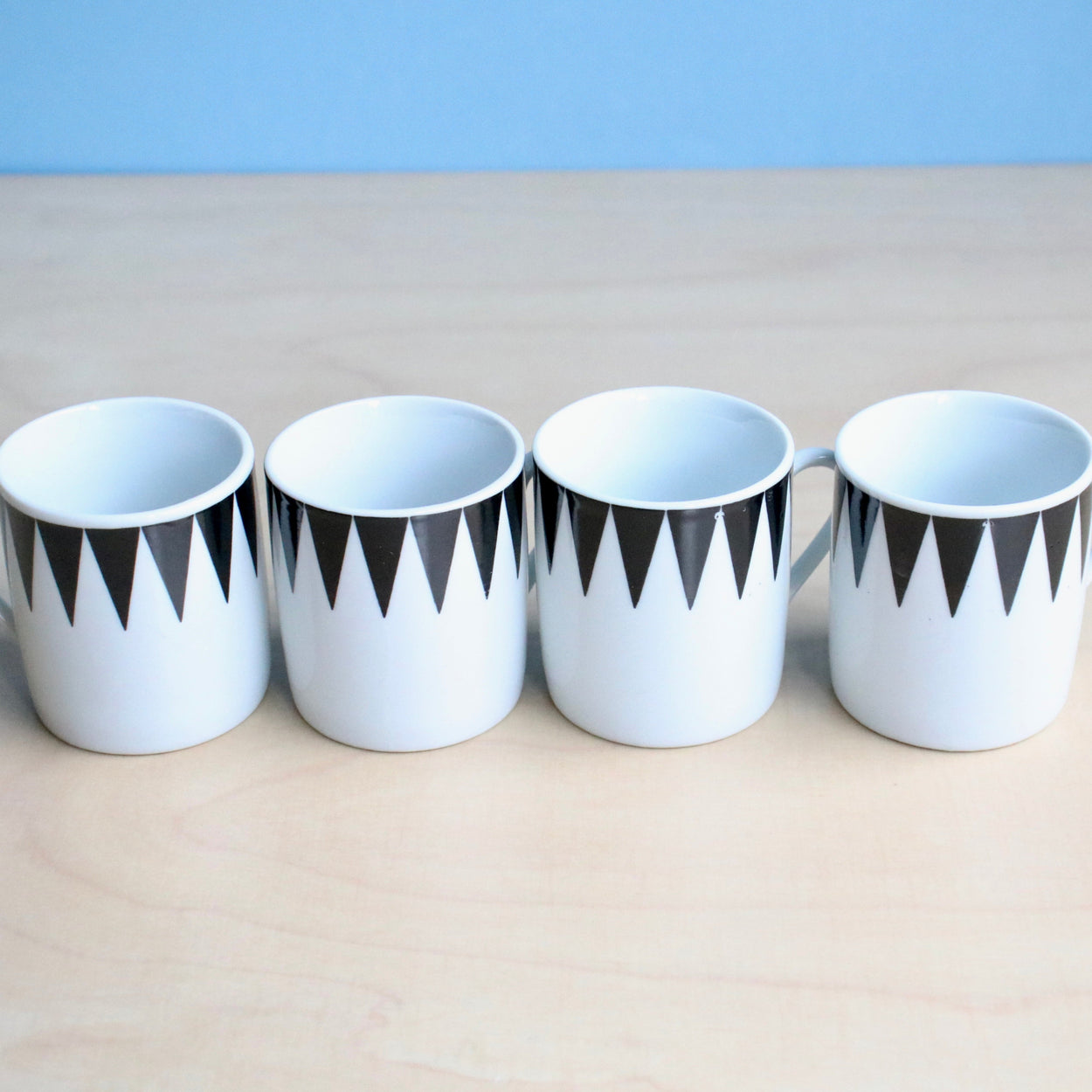 Four white espresso cups with black geometric patterns on a beige surface and light blue background