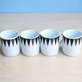Four white espresso cups with black geometric patterns on a beige surface and light blue background