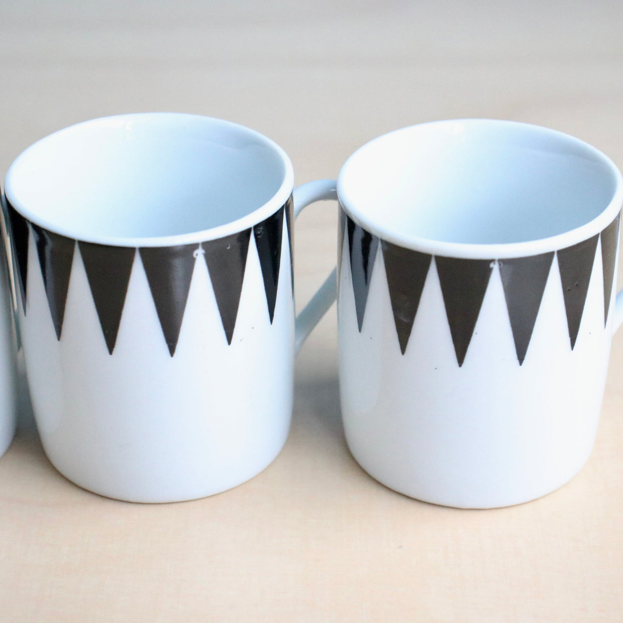 Two white espresso cups with black geometric patterns on a light background
