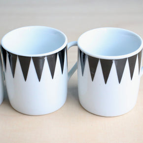 Two white espresso cups with black geometric patterns on a light background