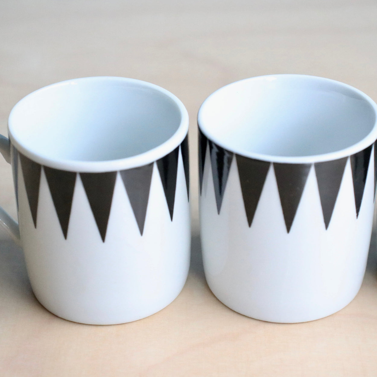 Two white cups with black geometric patterns on a beige background