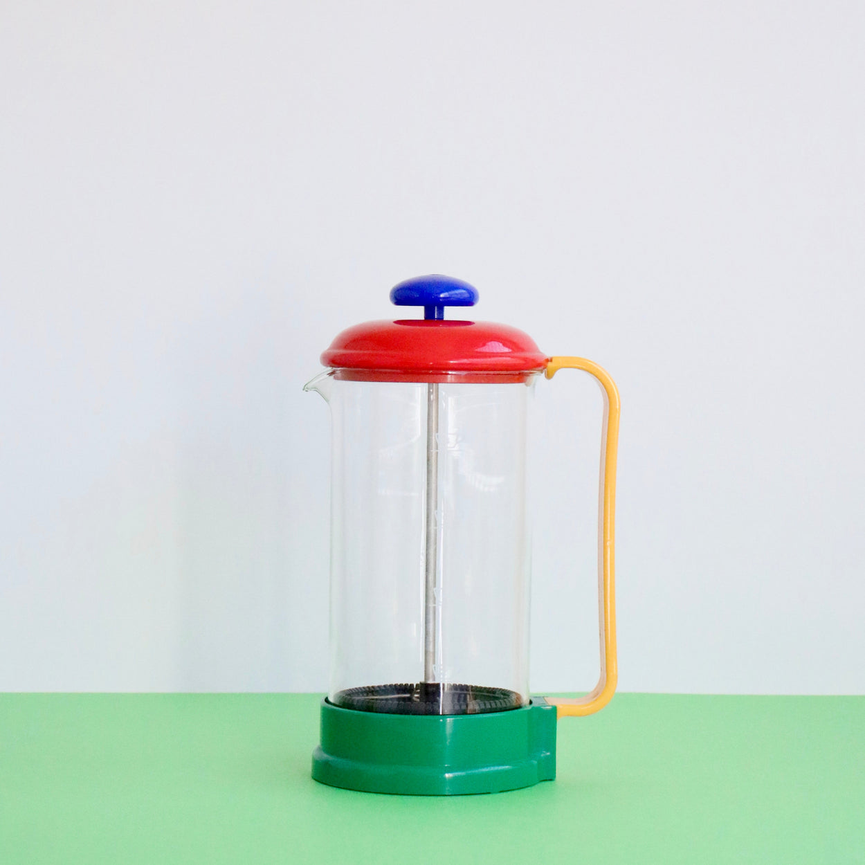 Colorful French press coffee maker on a green surface with a white background