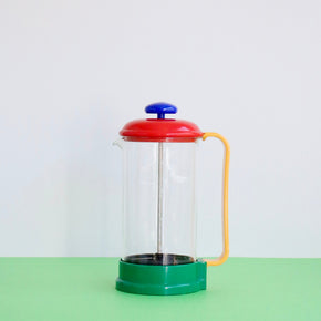Colorful French press coffee maker on a green surface with a white background