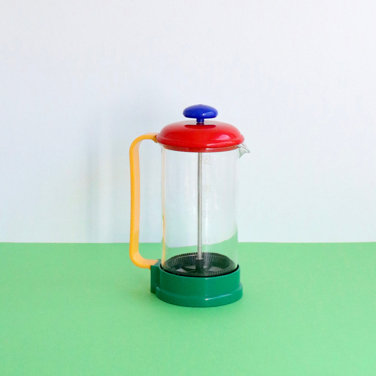 Colorful French press coffee maker on a green surface with a white background