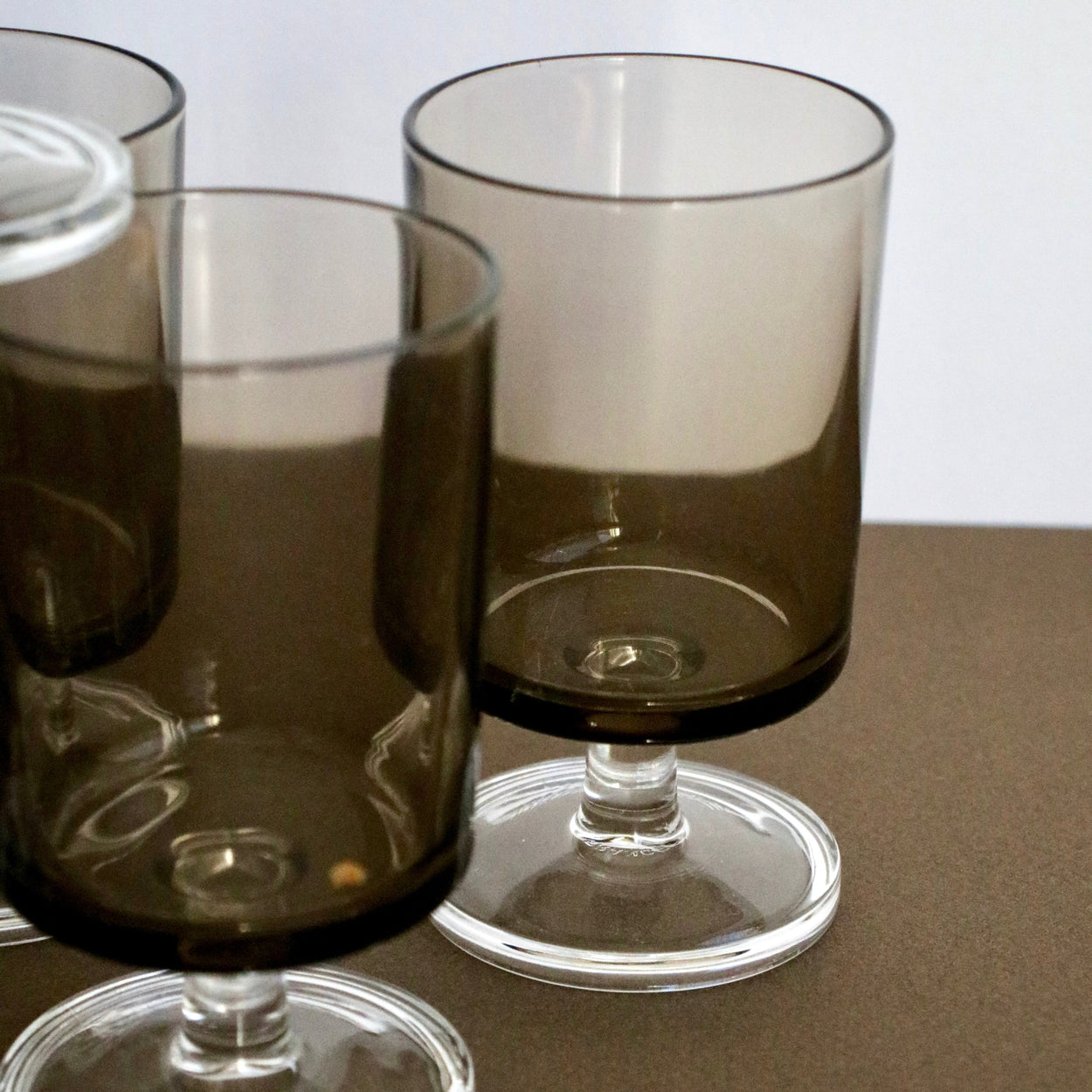 Two dark-tinted wine glasses on a brown surface with a neutral background