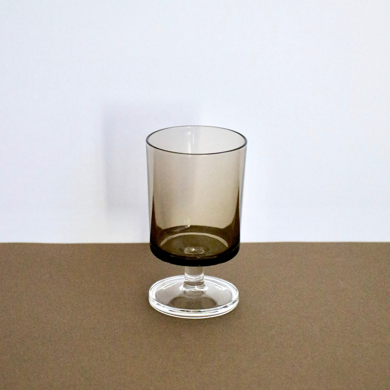 Smoky glass tumbler on a brown surface with a white background