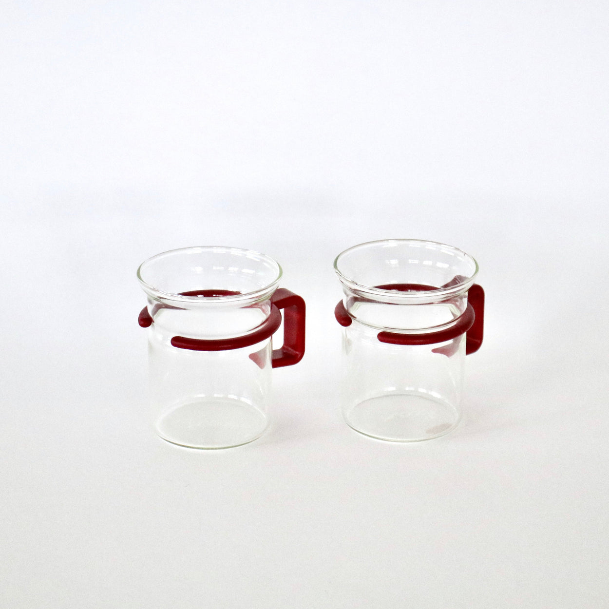 Two clear glass mugs with red handles on a white background