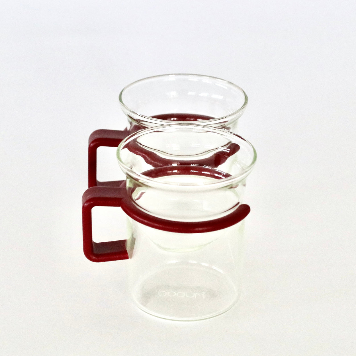 Clear glass coffee mugs with red plastic handles on a white background