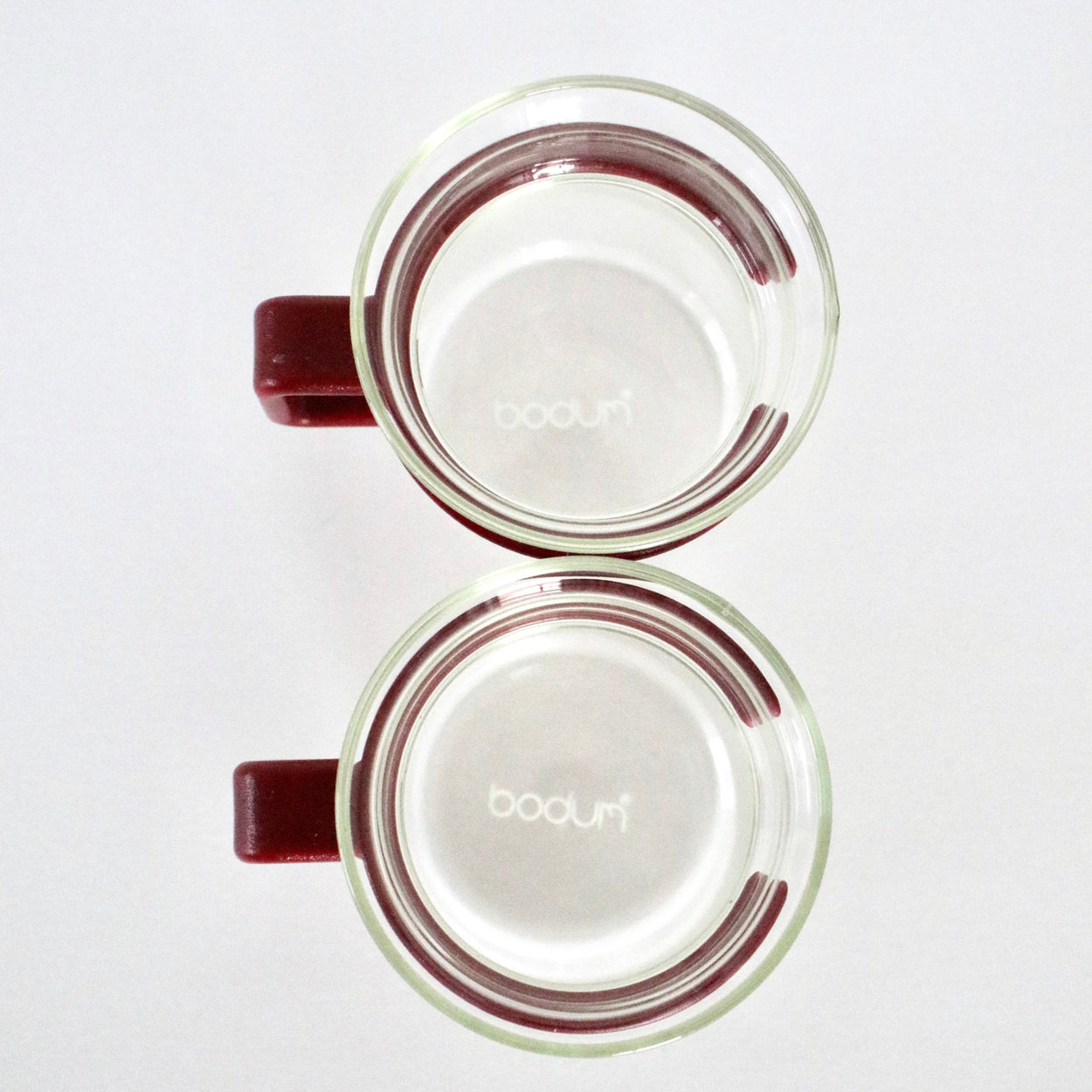 Two glass mugs with red handles on a white background