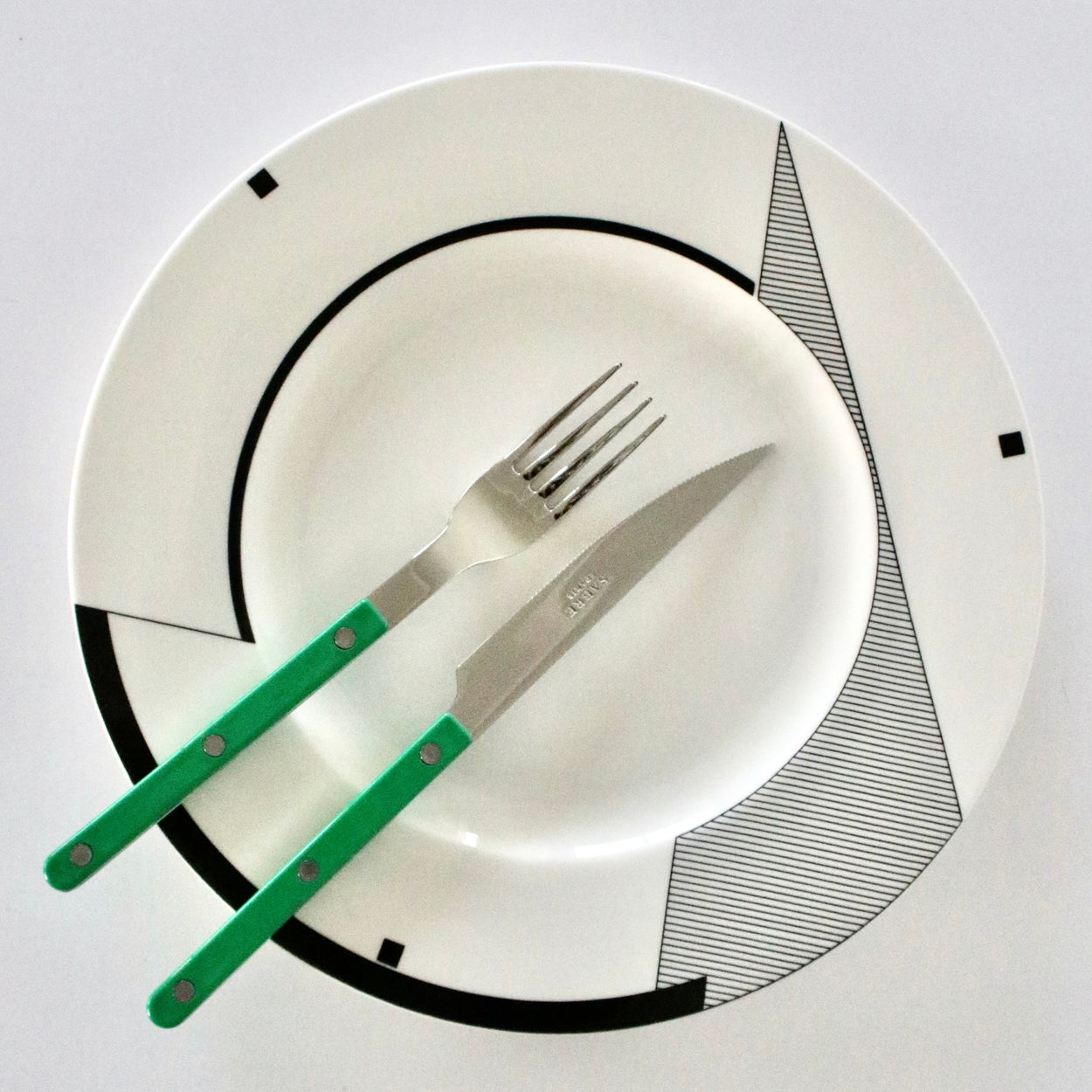 White plate with black geometric patterns, green knife, and silver fork on a white background