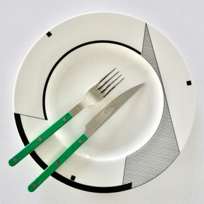 White plate with black geometric patterns, green knife, and silver fork on a white background