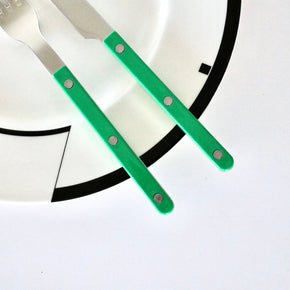 Two pieces of Sabre Paris Bistrot flatware with green handles on a white and black plate.