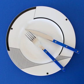 White plate with black geometric design, blue knife, and fork on a blue background
