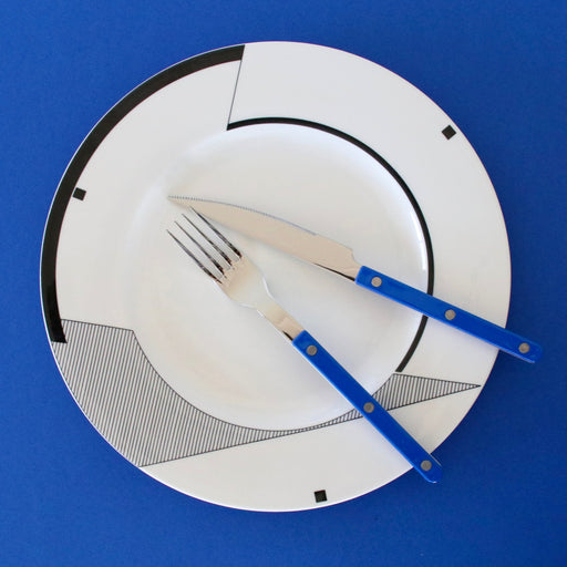 White plate with black geometric design, blue knife, and fork on a blue background
