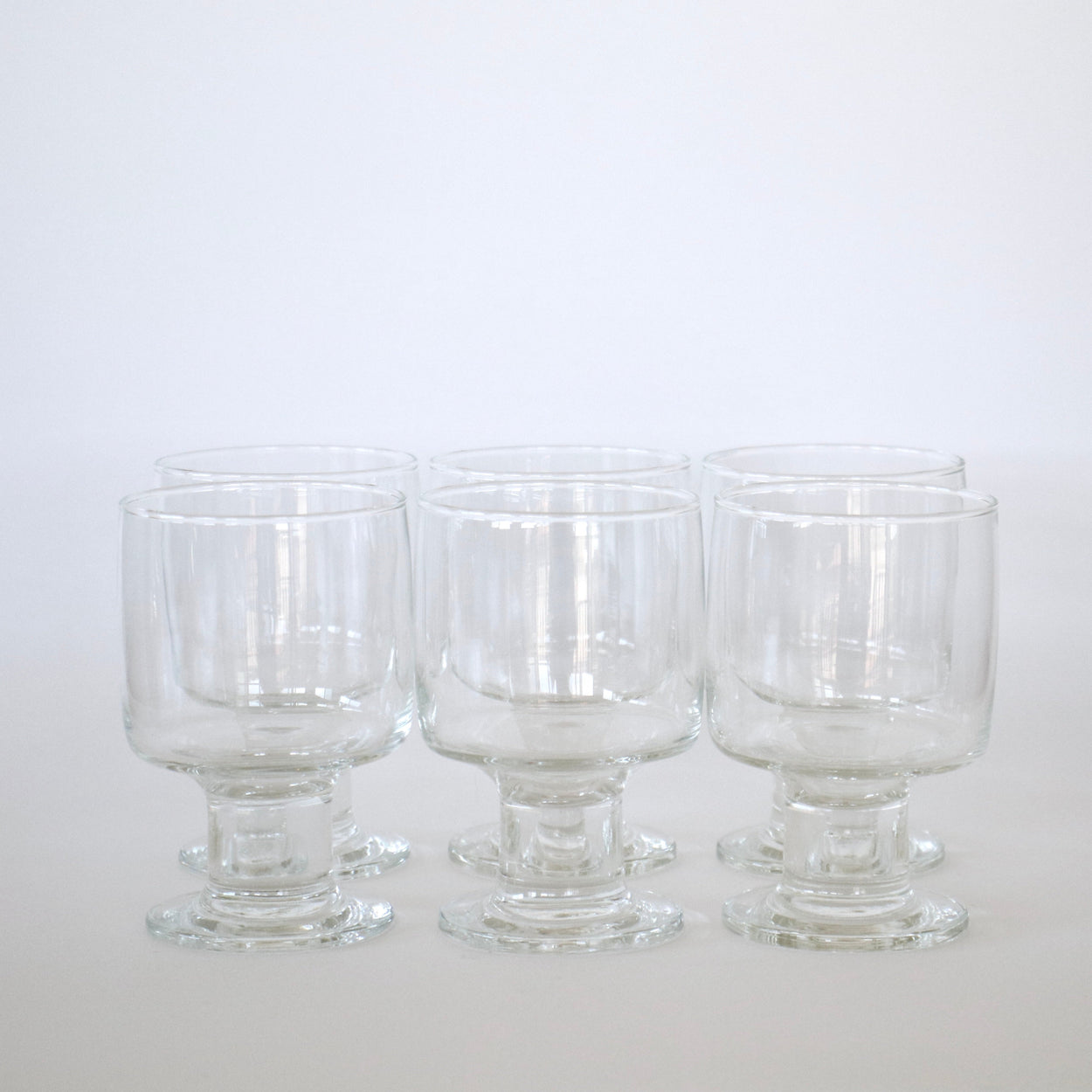 Six clear glass goblets on a white background