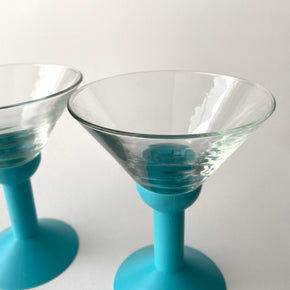 Two clear glass cocktail glasses with blue stems on a white background