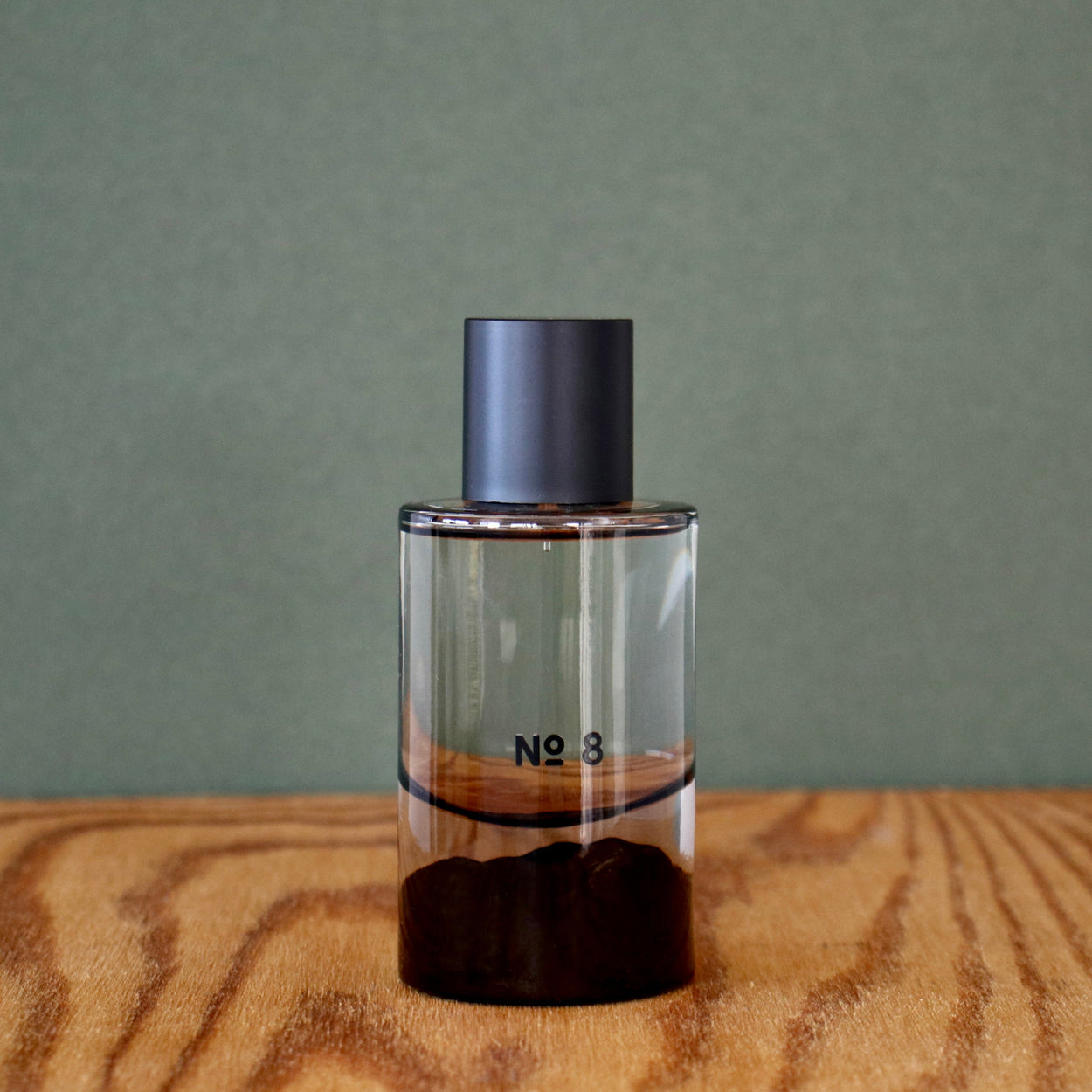 Clear perfume bottle with dark cap labeled 'No. 3' on a wooden surface with a green background