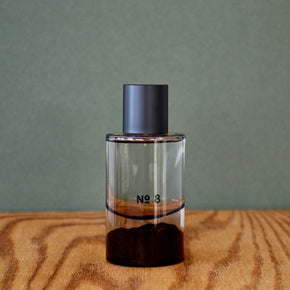 Clear perfume bottle with dark cap labeled 'No. 3' on a wooden surface with a green background