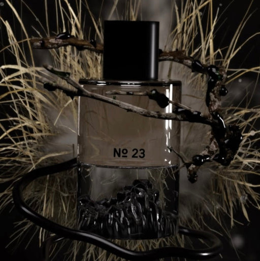 Perfume bottle labeled 'No. 23' surrounded by grass and branches on a dark background
