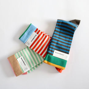 Three pairs of striped socks from Bonne Maison arranged on a plain white background. The socks feature various stripe patterns including blue and black, red and white, and green and white, with one pair showing a brown and orange base.