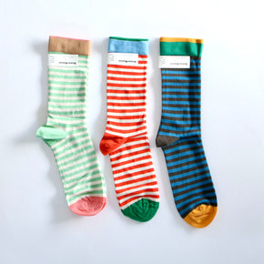 Three pairs of striped crew socks laid flat on a white background. The left pair is mint green and white striped with a pink toe and a brown cuff.