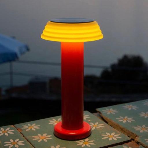 Sowden PL1 rechargeable outdoor lamp with yellow top and red base on a table with a floral pattern.