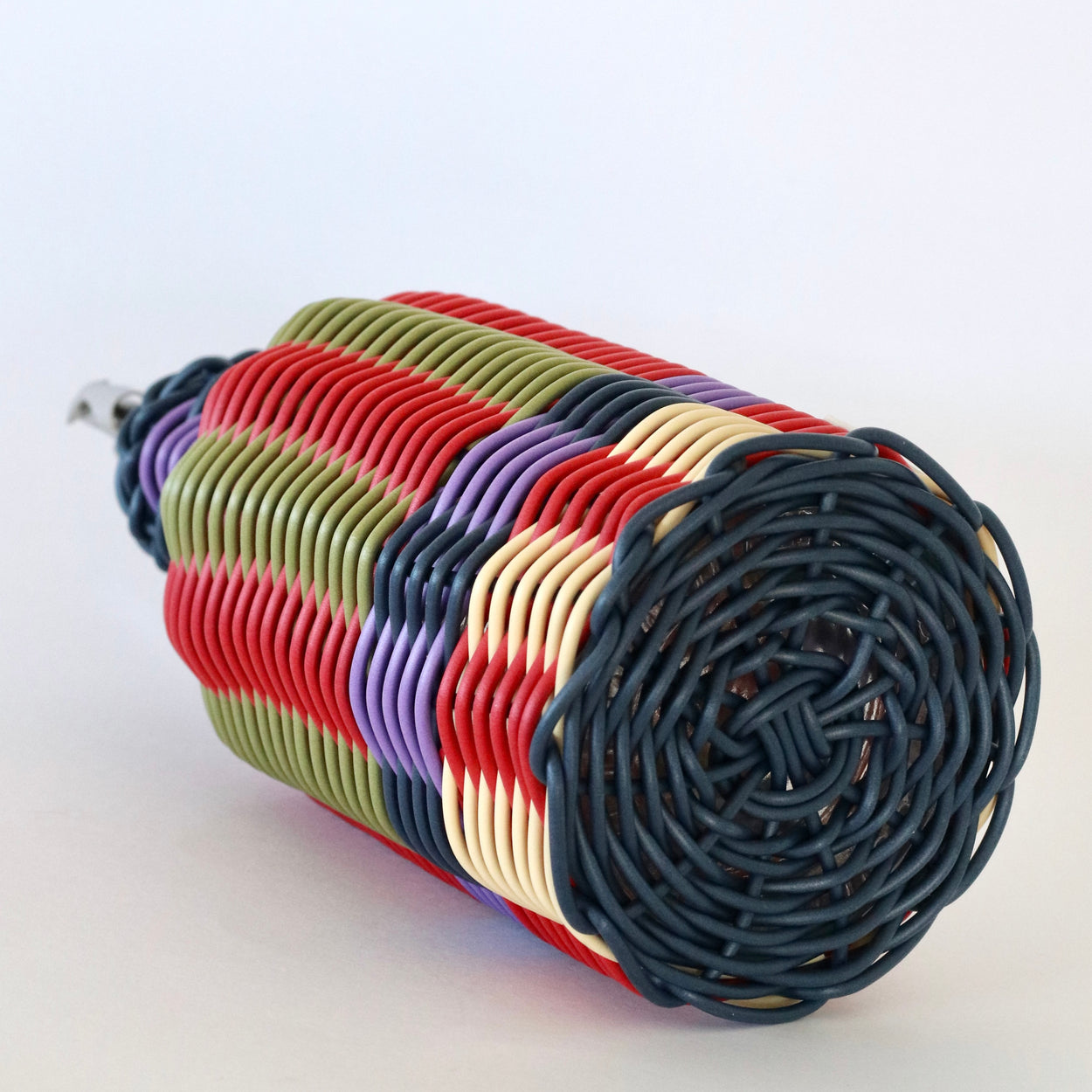Base of Decorative olive oil bottle with blue, red, green  and cream woven design and metallic nozzle on a white background