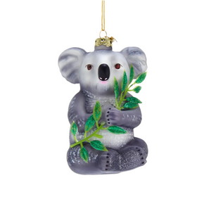Glass koala ornament holding eucalyptus leaves on a white background