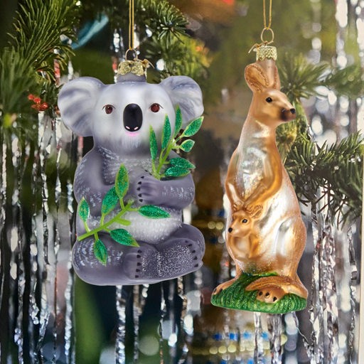 Two Christmas ornaments, a koala and a kangaroo, hanging on a decorated tree.