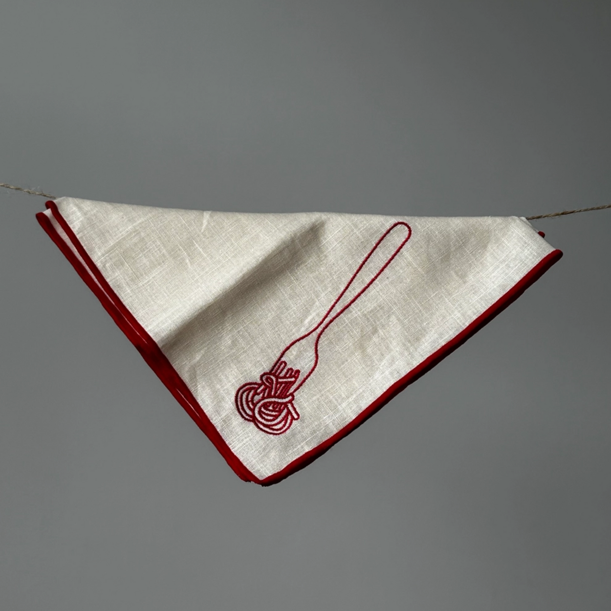 White napkin with red border and embroidered design on a gray background