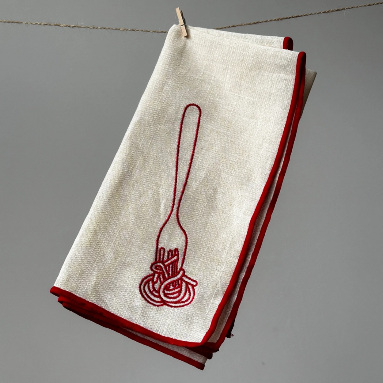 White napkin with red embroidered design of a fork and spaghetti on a gray background