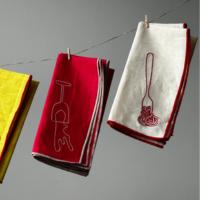 Colorful napkins with embroidered designs hanging on a line against a gray background