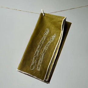 Green napkin with white embroidery hanging on a line against a gray background