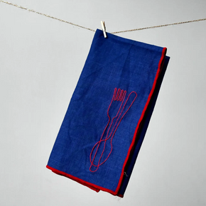 Blue napkin with red trim and embroidered fork and knife on a gray background