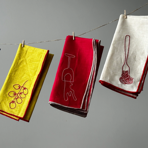 Colourful napkins with embroidered designs hanging on a line against a gray background