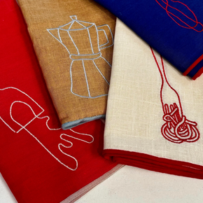 Four folded linen napkins in red, tan, blue, and cream, each featuring a minimalist embroidered kitchen utensil or food outline in contrasting thread.