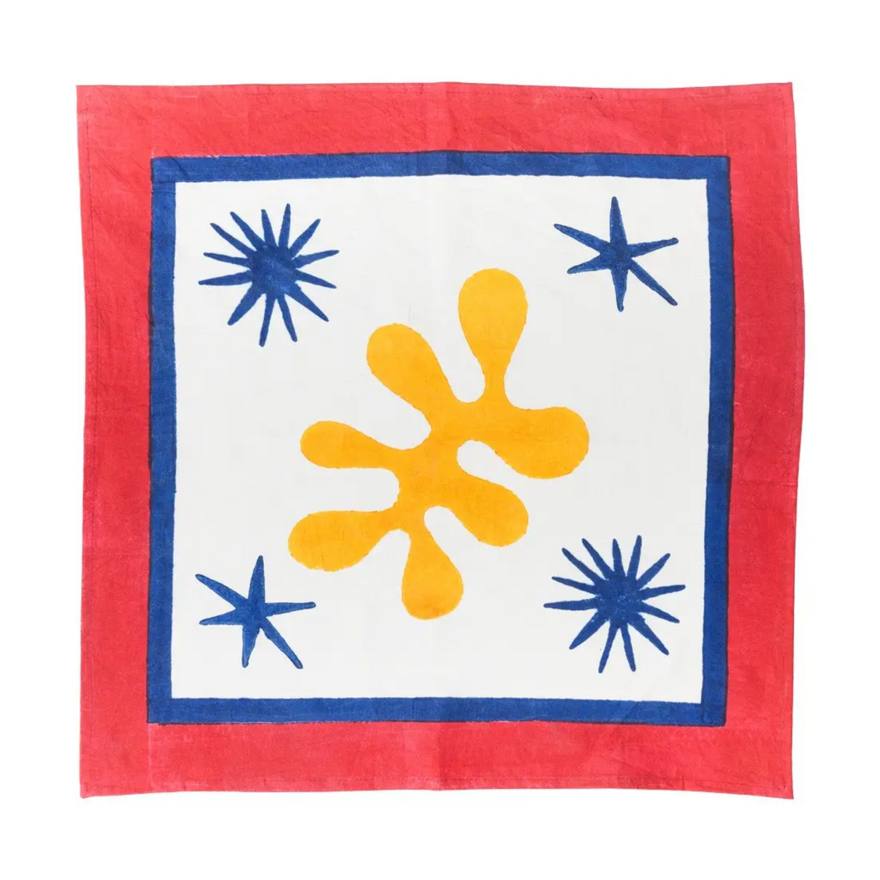 A square textile napkin, featuring a bold abstract design. The fabric has a solid red border, a white center, a thick blue inner border, a large yellow-orange splatter motif in the middle, and three blue starburst accents in the corners.