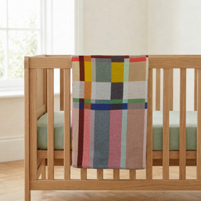Colorful plaid blanket draped over a wooden crib in a bright room.