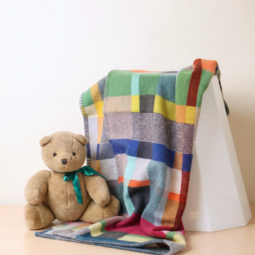 Multicolored checkered blanket draped over a white surface with a teddy bear sitting on it.