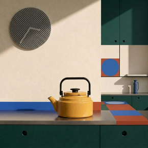Yellow teapot on a kitchen counter with colorful cabinets and a clock in the background