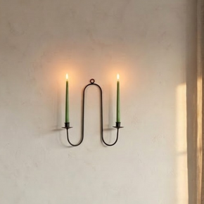 Wrought iron wall sconce with two candles on a neutral wall.