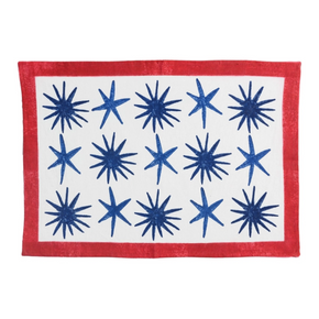 A rectangular textile placemat or table mat with a red border, a white center, and blue starburst motifs arranged in a grid.