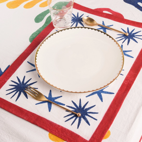 Colorful tablecloth with abstract patterns and a white plate with gold rim. Matching placemat below plate.