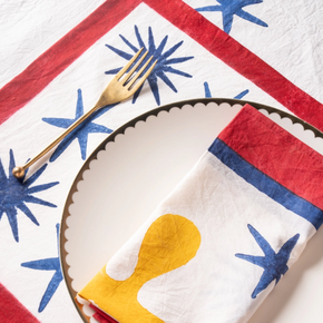 Napkin with yellow organic design on a plate, placed on a red, white, and blue patterned tablecloth.